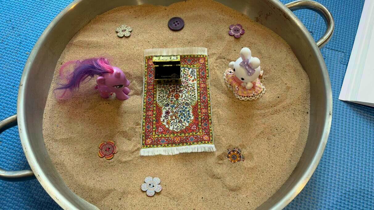A small tray of sand containing a pony, bunny figure, prayer rug, and decorative elements