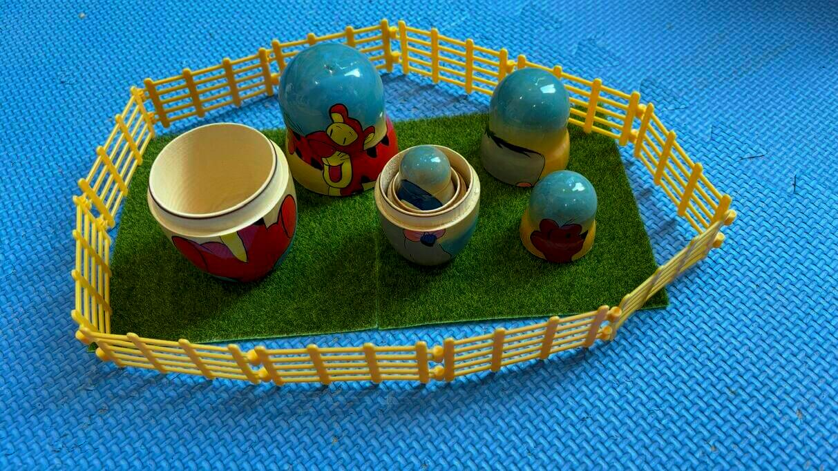 A set of colourful nesting dolls arranged within a yellow fence on artificial grass