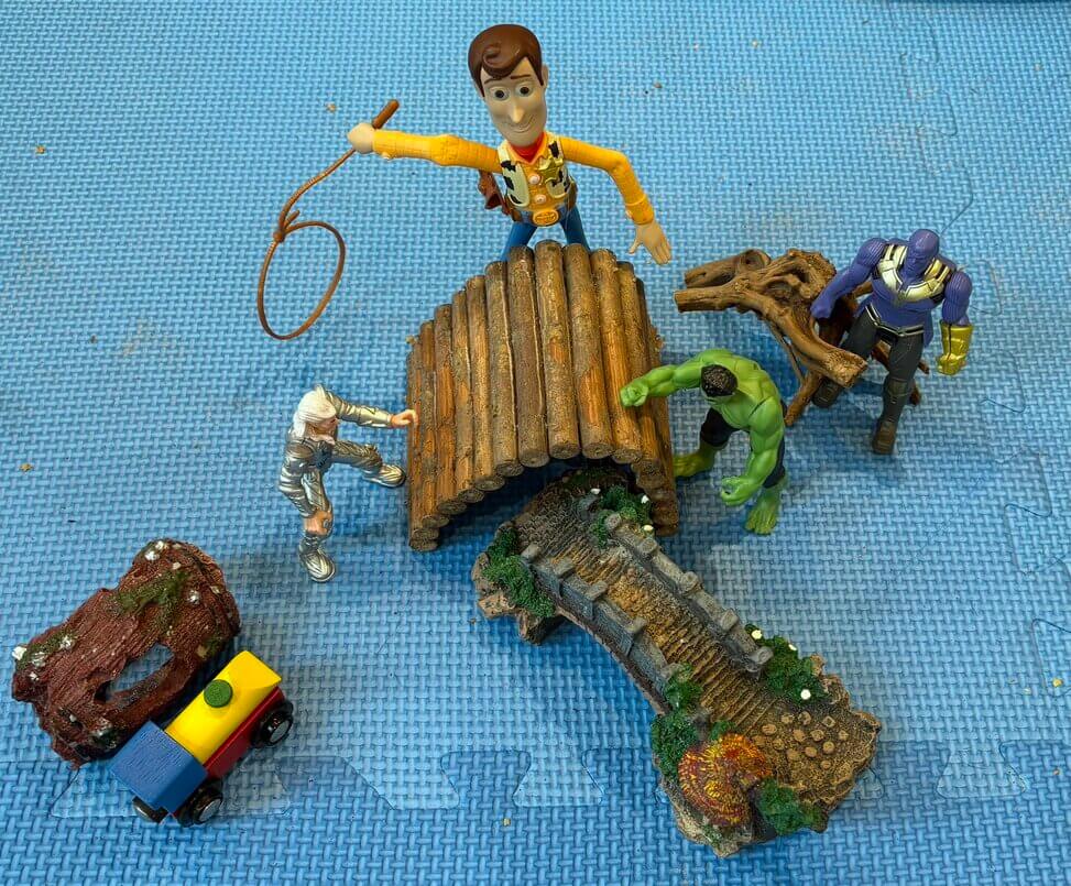 Toy figures crossing bridges and interacting, including superheroes and familiar characters like Woody and Hulk