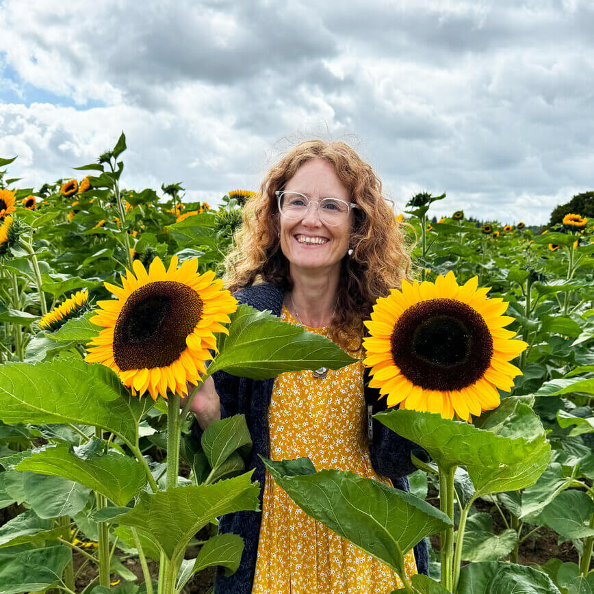 Natasha standing in a sunflower field, smiling warmly.