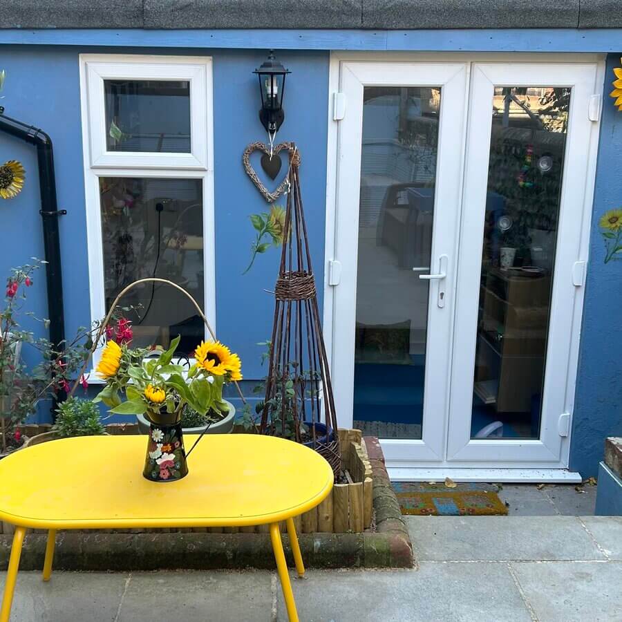 Outside the Sunflower House play therapy studio, with vase of sunflowers on a yellow table.